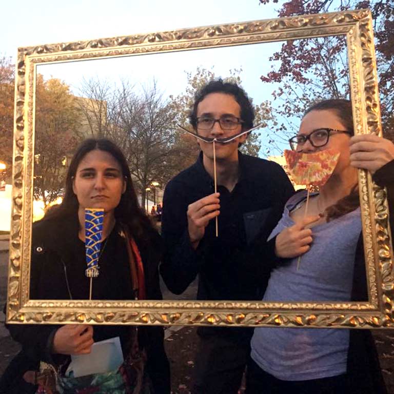Three students pose with props inside a picture frame.